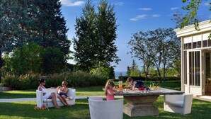 A patio area with outdoor furniture, a table, and a view of the surrounding garden and trees.