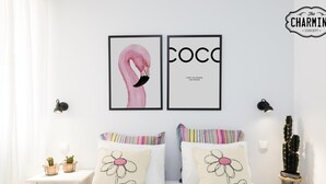 A bedroom with a white bed, two pillows with floral designs, a framed artwork of a flamingo and the word "COCO", and a cactus on a nightstand. - Madrid City - Two-bedroom apartment (Madrid)