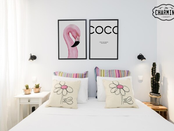 A bedroom with a white bed, two pillows with floral designs, a framed artwork of a flamingo and the word "COCO", and a cactus on a nightstand. - Madrid City - Two-bedroom apartment (Madrid)