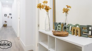 A hallway with a white console table displaying a welcome sign, vases with flowers, and a wooden tray. - Madrid City - Two-bedroom apartment (Madrid)