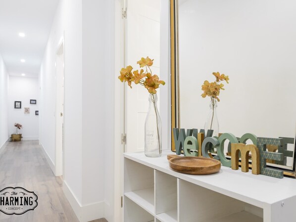 A hallway with a white console table displaying a welcome sign, vases with flowers, and a wooden tray. - Madrid City - Two-bedroom apartment (Madrid)