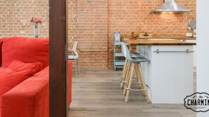 A modern kitchen with a brick wall, a red sofa, and a bar area with stools. - Madrid City - Two-bedroom apartment (Madrid)