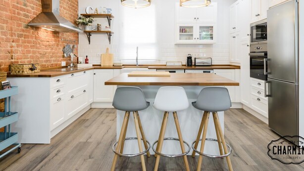 A modern kitchen with white cabinets, a brick accent wall, and a central island with bar stools. - Madrid City - Two-bedroom apartment (Madrid)