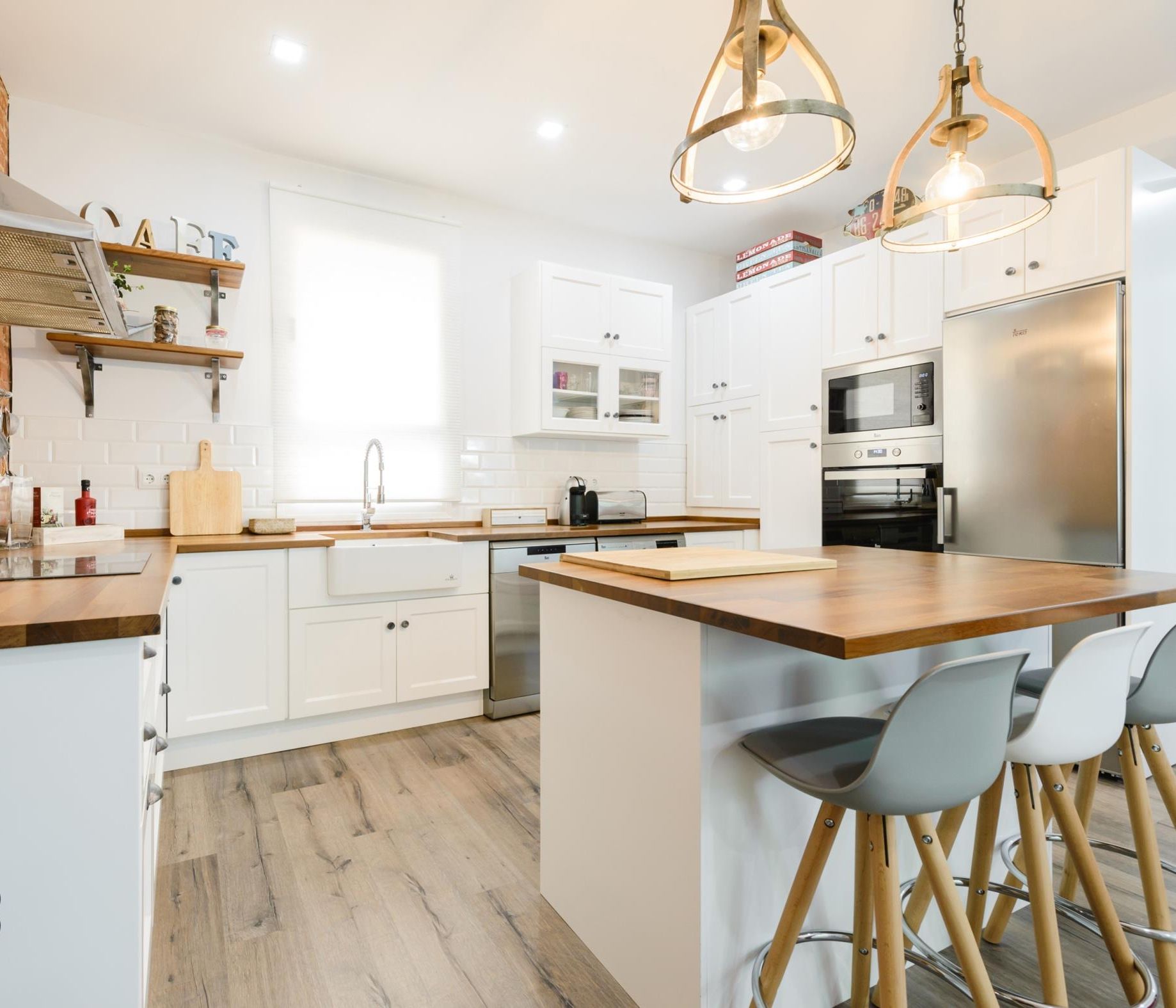 Een moderne keuken met witte kasten, een houten keukeneiland, roestvrijstalen apparatuur en een accentmuur van baksteen.