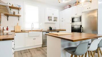 Een moderne keuken met witte kasten, een houten keukeneiland, roestvrijstalen apparatuur en een accentmuur van baksteen.
