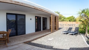 A modern house with a covered patio, a wooden table and chairs, and a small garden area with a pool and lounge chairs. - Casa Cristina, new modern apartment in Lajares, Fuerteventura (Lajares)