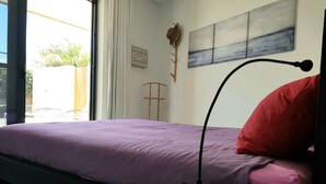 A bedroom with a bed, a bedside table, a lamp, a window, and a wall with a painting. - Casa Cristina, new modern apartment in Lajares, Fuerteventura (Lajares)