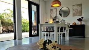 A modern living room with a concrete coffee table, white furniture, and a view of a garden through large glass doors. - Casa Cristina, new modern apartment in Lajares, Fuerteventura (Lajares)