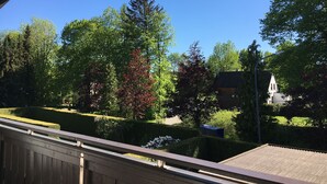 Une vue depuis un balcon donnant sur un jardin bien entretenu, avec différents arbres et un bâtiment en arrière-plan.
