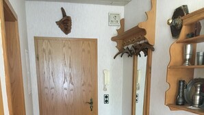 Un couloir avec une porte en bois, une chaise, un tapis et un meuble en bois doté d’étagères.