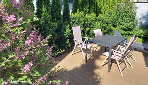 En udendørs patio med et bord og stole, omgivet af frodigt grønt og blomstrende planter.