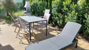 Um terraço com mesa, cadeiras, uma espreguiçadeira e uma churrasqueira.