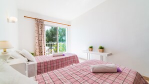 Une chambre avec deux lits, une fenêtre avec des rideaux, une petite table avec des plantes et une table de chevet avec une lampe.