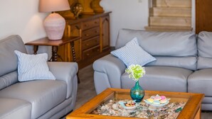 Un salon avec deux canapés gris, une table basse en bois sur laquelle se trouvent un vase et des pâtisseries, et un escalier en arrière-plan.