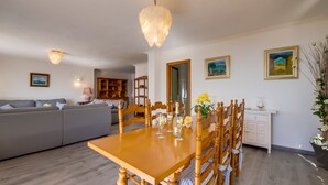 Un coin repas avec une table et des chaises en bois, un lustre et un canapé en arrière-plan.