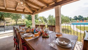 A wooden dining table set for breakfast with a view of a swimming pool and greenery. - Rural Villa in Mallorca Ses Comes with pool (Selva)