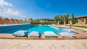A swimming pool with lounge chairs and pillows, surrounded by a tiled patio and greenery. - Rural Villa in Mallorca Ses Comes with pool (Selva)