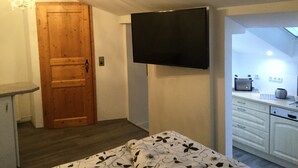 A bedroom with a bed, a wooden door, a TV mounted on the wall, and a skylight above. - Apartment Fernblick near Rosalie  (Ottobeuren)