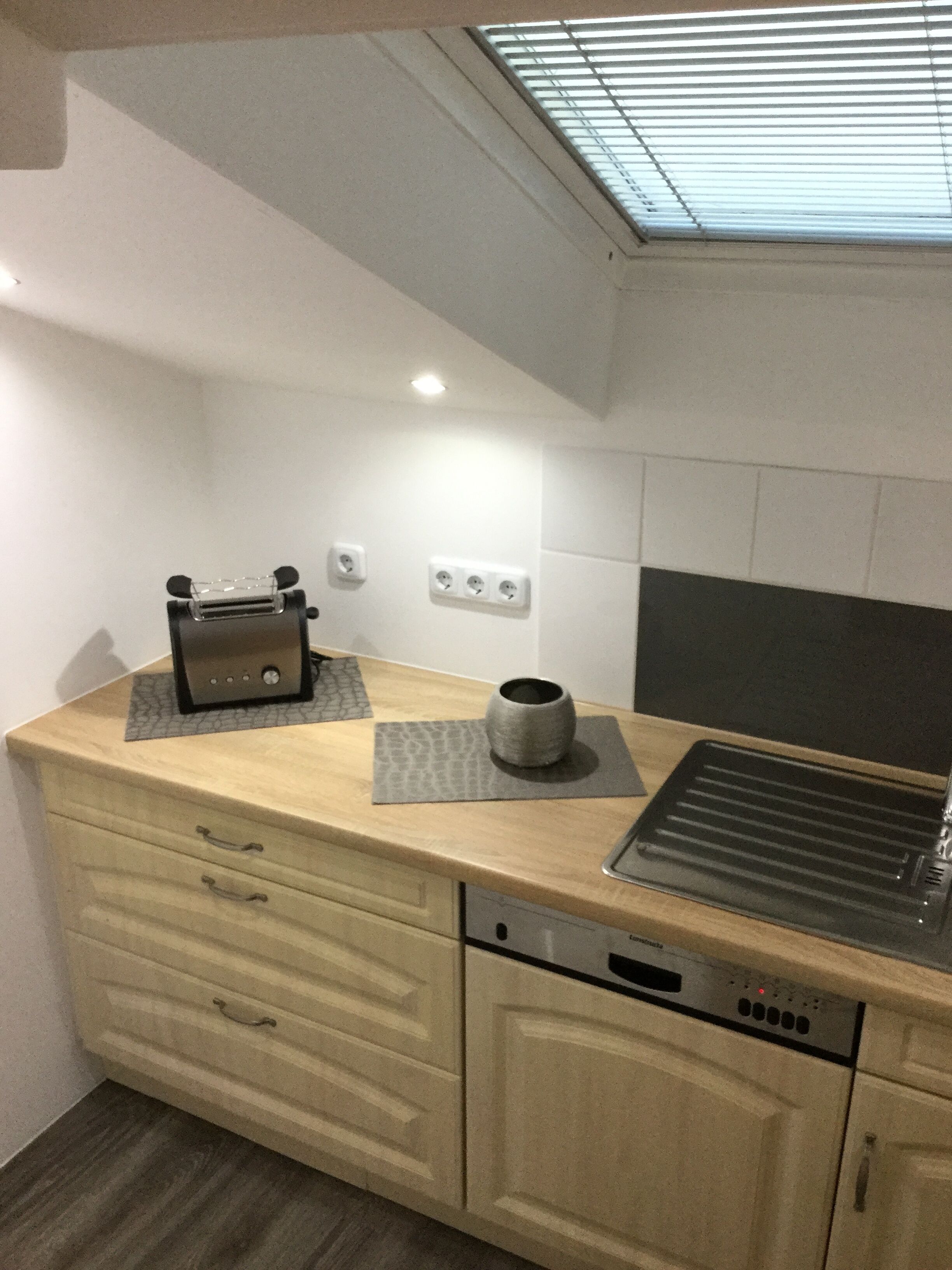 A compact kitchen with a toaster, a coffee cup, and a dishwasher.
