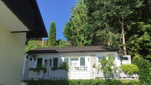 A white house with a tiled roof, surrounded by dense greenery and tall trees. - Apartment Fernblick near Rosalie  (Ottobeuren)