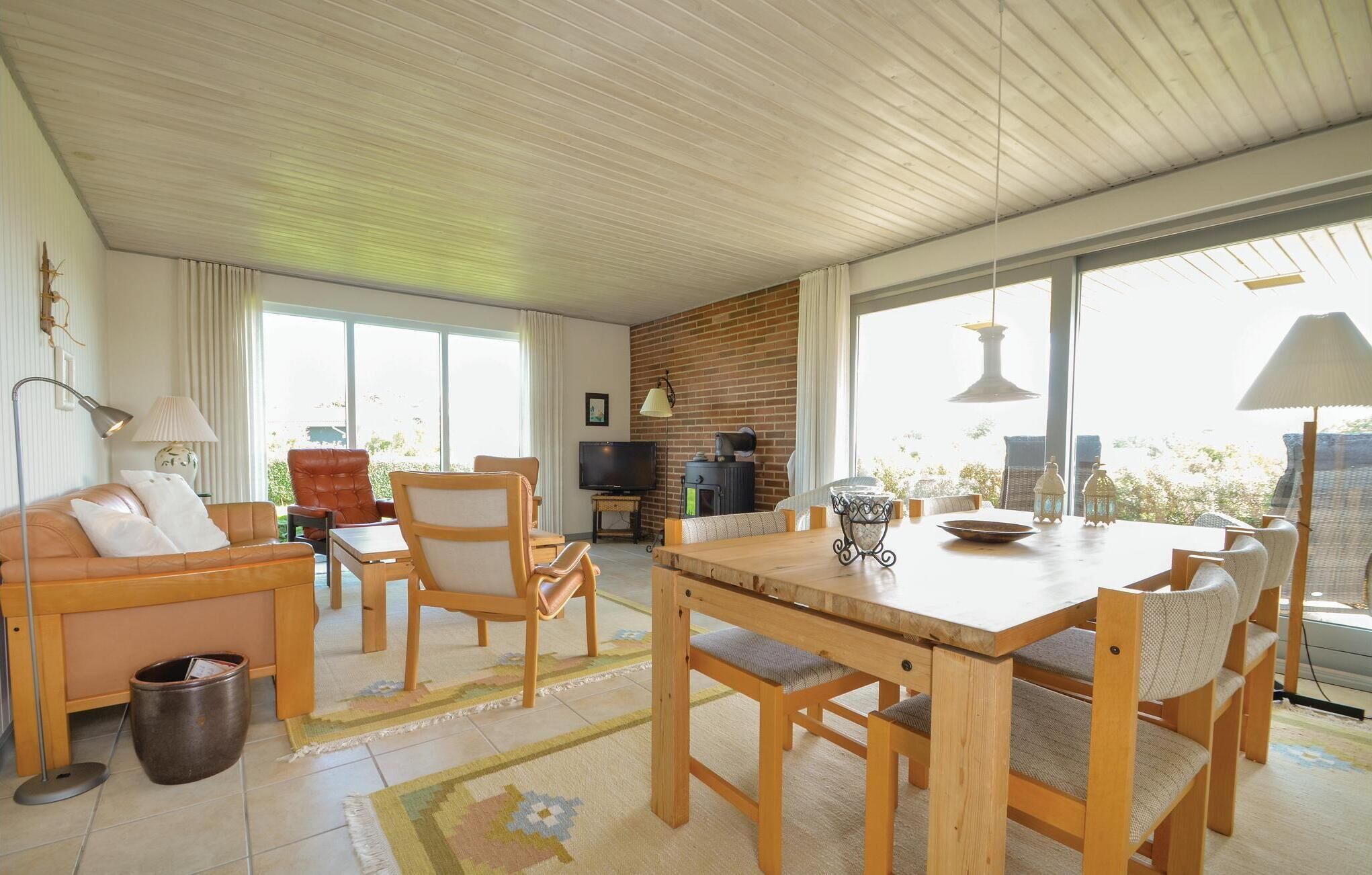 Ein großzügiges Wohnzimmer mit einem Holzespeisetisch, bequemen Sitzmöglichkeiten, einem Fernseher und großen Fenstern mit Blick ins Freie.