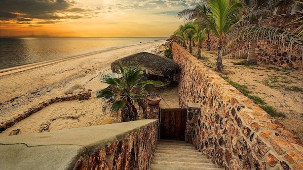 A stone staircase leading down to a beach with palm trees and a sunset in the background. -  Secluded Beach Front Estate with a Large Pool, Family and Pet Friendly!  (Los Barriles)