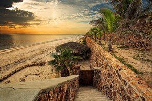 A stone staircase leading down to a beach with palm trees and a sunset in the background. -  Secluded Beach Front Estate with a Large Pool, Family and Pet Friendly!  (Los Barriles)