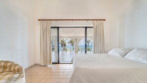 A bedroom with a large bed, a sofa, and a sliding glass door leading to a balcony with a view of palm trees and the sea. -  Secluded Beach Front Estate with a Large Pool, Family and Pet Friendly!  (Los Barriles)