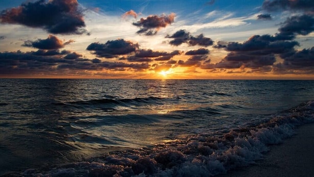 A sunset over the ocean with waves crashing onto the shore. - Best Value in Clearwater/ St. Pete Region! (Madeira Beach)