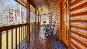 A wooden cabin with a porch, wooden railings, and a view of a forest.