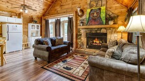 A cozy cabin interior with a fireplace, wooden walls, a dining area, and a living room with two sofas.