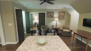 Un salón con un tapete grande y estampado, dos sillones, una mesita con una lámpara y un televisor en la pared.