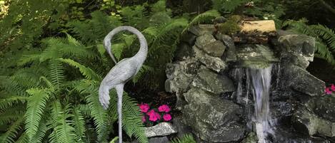 Un jardin agrémenté d’une fontaine en pierre, de fougères et d’un seau en métal.
