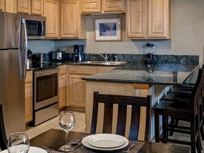 A kitchen with wooden cabinets, stainless steel appliances, a granite countertop, and a dining area with a table and chairs.