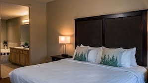 Une chambre d’hôtel avec un grand lit, une table de chevet, une lampe, un miroir et une salle de bain visible au fond.