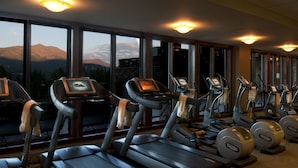 Une salle de sport équipée de tapis de course et d’appareils elliptiques, de grandes fenêtres offrant une vue sur les montagnes et de divers équipements d’exercice.