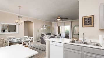 A modern kitchen with a dishwasher, a dining area with a white table and chairs, and a ceiling fan.