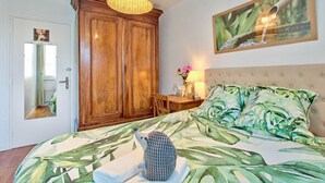 A bedroom with a large bed, a wooden wardrobe, a dining table, and a mirror. - “L’Authentique”: soothing and rural! Air conditioning and free/secure parking! (Villeurbanne)