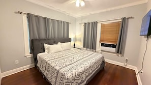 Un dormitorio con una cama, una mesita de noche, una lámpara y un ventanal con cortinas.