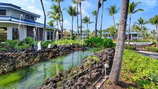 A resort with a pool surrounded by palm trees and a house with a blue roof. -  Spacious, Luxurious, Tropical Townhouse Style Condo For A Truly Aloha Vacation (Kailua-Kona)