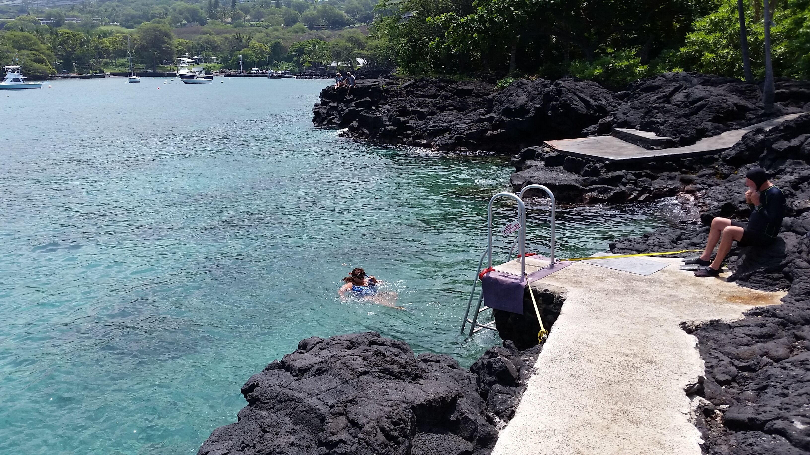 A clear view of a swimming pool with a diving board, surrounded by rocky terrain and clear water.