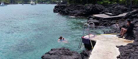 A clear view of a swimming pool with a diving board, surrounded by rocky terrain and clear water.
