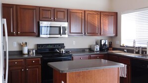 A kitchen with wooden cabinets, a microwave, stove, toaster, and coffee maker. - Classy and Comfortable, Gated 4-Bdrm Home, Heated Pool Family-Friendly (Mesa)