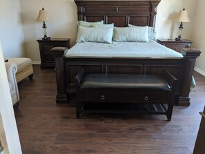 A large bed with a wooden headboard, two bedside tables with lamps, a bench at the foot of the bed, and a chair in the corner.