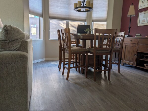 A dining area with a wooden table and chairs, a laptop on the table, and a lamp on a cabinet.