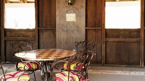 A wooden ceiling with exposed beams, a round table with a checkered tablecloth, and metal chairs with striped cushions.