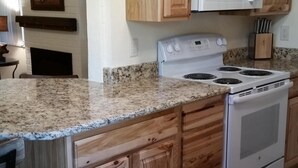 A kitchen with wooden cabinets, a granite countertop, a white microwave, and a stove.