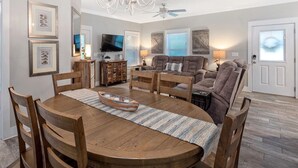 Un coin repas comprenant une table en bois, des chaises, un lustre et un téléviseur.