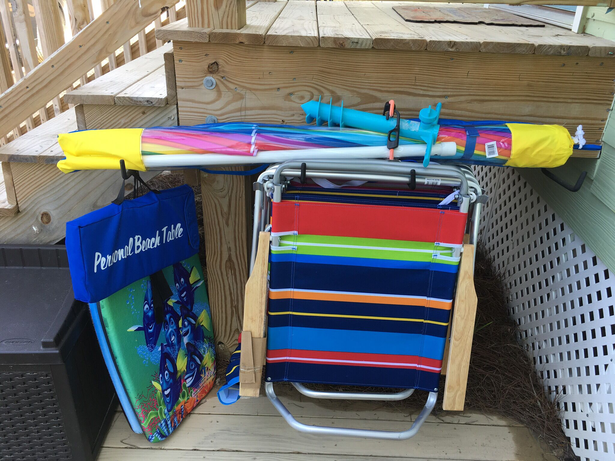 A wooden deck with a colorful beach towel, a blue bag labeled "Personal Beach Table," and a metal chair.