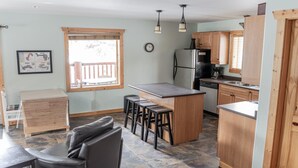 A compact kitchen with a central island, wooden cabinets, a refrigerator, and a dining area with stools. - Legacy Vacation Rental - Pet Friendly! (Valemount)